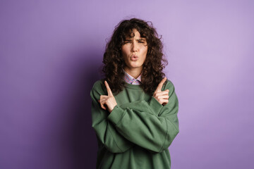 Happy beautiful curly girl grimacing and pointing her fingers upward
