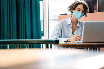 Pleased girl writing down notes while working with laptop