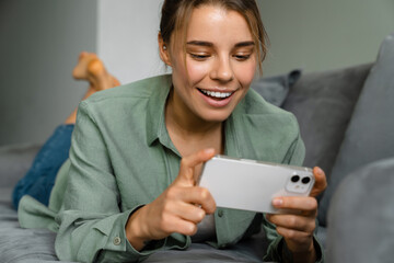 Happy nice woman using mobile phone while lying on sofa