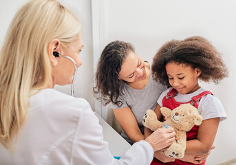 Pediatrician holds a stethoscope, communicates with a little girl patient. Visiting child doctor with mother, kid health