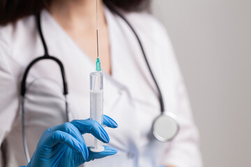 Woman holding medical injection syringe in her outstretched hand towards the camera.