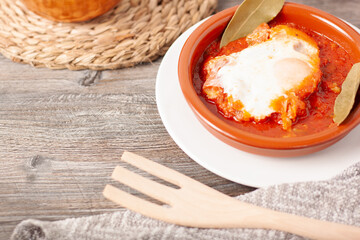 Concepto de un plato de barro con una parte superior de tomate frito, carne de cerdo magra y un huevo estrellado con un tenedor de madera