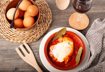 concepto de un plato de barro con una tapa de tomate frito, cerdo magro y un huevo estrellado con un tenedor de madera y una copa de vino en una mesa tradicional vista desde arriba.