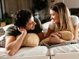 Young loving couple relaxing on bed together. Happy couple watching movie at home..