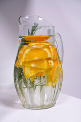 Glass decanter with a refreshing soft drink made from orange and basil slices on a light background