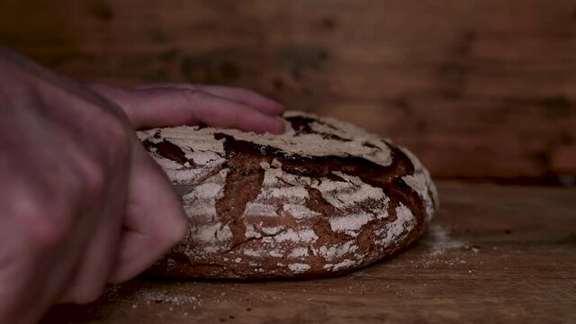 Cut crispy handmade bread into slices. Hands slice round crust bread on rustic wooden table. Close-up slow motion movie with sound