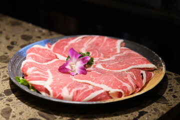 Close up slice of raw beef in plate. Raw food for hot pot. Blurred dark background