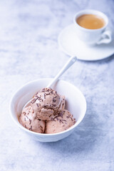 Chocolate ice cream with chocolate sprinkle in a white bowl on a light background. Three balls of homemade ice cream and a cup of coffee. Close-up.