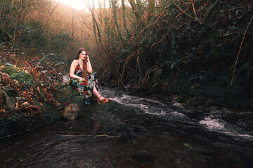 Young caucasian woman with a colorful dress in the middle of the forest next to a little river