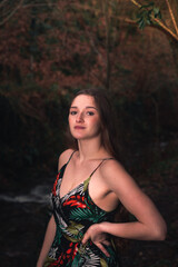 Fototapeta na wymiar Young caucasian woman with a colorful dress in the middle of the forest next to a little river