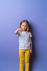 little cute Caucasian girl of 5 years old, offended and pouted on a purple background. The baby is tired, mischievous, does not go to contacts and points with her finger. Close-up