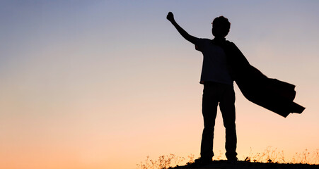 Boy playing superheroes on the sky background, teenage superhero in a red cloak on hill © Chepko Danil