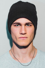 retrato de chico guapo de ojos claros. Joven caucásico con camiseta ancha y gorro. expresión serio y peligroso. (Modelo actor profesional en estudio)