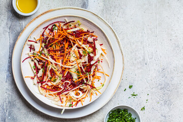 Beetroot, carrot, cabbage salad with oil and herbs, gray background. Healthy food concept.