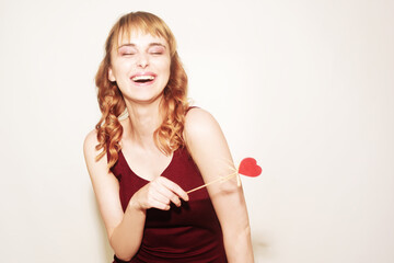 A beautiful brunette holds a heart on sticks in her hands, women's day, March 8, holiday. Happy girl on a white background smiles.