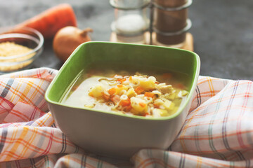 Chicken noodle soup with vegetables in a green plate, black background