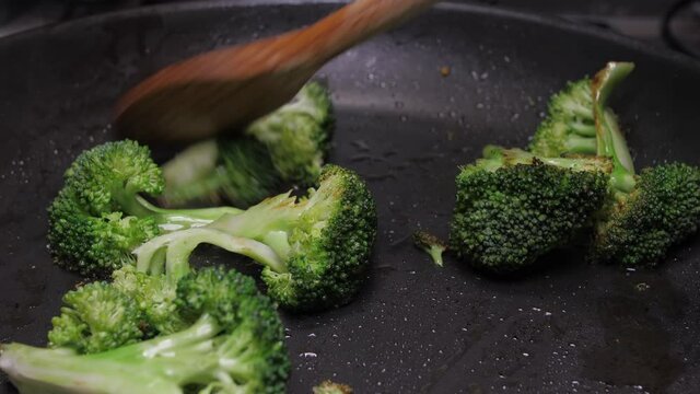 mixing broccoli with wood spoon on oil fry pan 4k