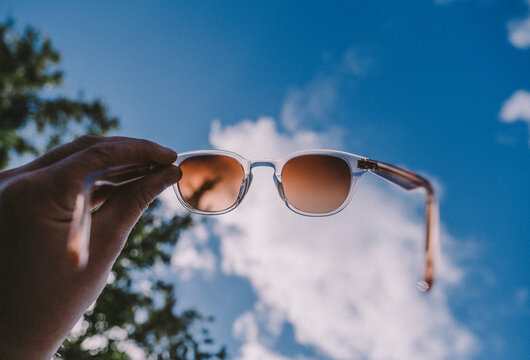 Hand holding sunglasses against sky