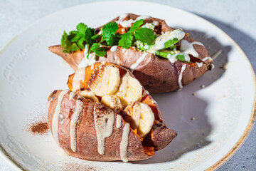 Whole baked sweet potatoes stuffed with avocado and banana on gray plate. Plant based food concept.