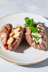 Whole baked sweet potatoes stuffed with avocado and banana on gray plate. Plant based food concept.