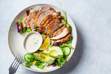 Grilled chicken salad with avocado, cucumber and dressing, top view. Healthy food concept.