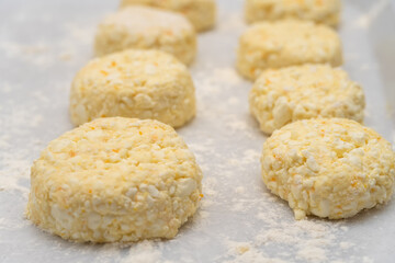 Lots of cottage cheese pancakes on a white tray with flour close up before frying in a frying pan. Selective Focus