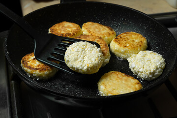 Cottage cheese pancakes are fried for breakfast in a black pan close-up. Flipping cottage cheese pancakes with a spatula