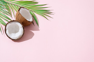 Fototapeta na wymiar Tropical green palm leaf and cracked coconut on pink background. Organic food, cosmetics. Trendy summertime banner, spa concept. flat lay, top view, copy space
