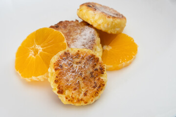 Three sweet curd cottage cheese pancake sprinkled with powdered sugar with two orange slices close-up on a white plate with the ability to copy the space. Concept of a delicious, healthy breakfast