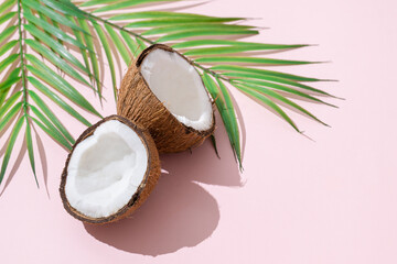 Fototapeta na wymiar Tropical green palm leaf and cracked coconut on pink background. Organic food, cosmetics. Trendy summertime banner, spa concept. flat lay, top view, close up