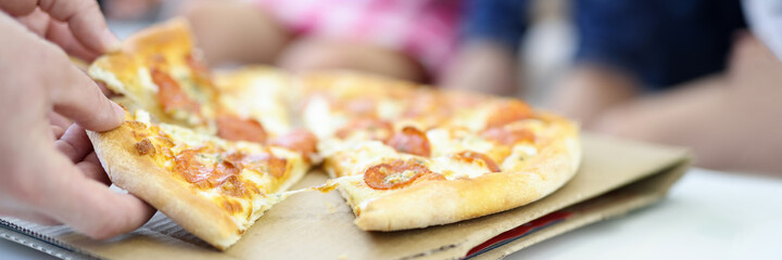 On table lies pizza, cut into pieces man's hand holds two piles. Cooking pizza at home concept