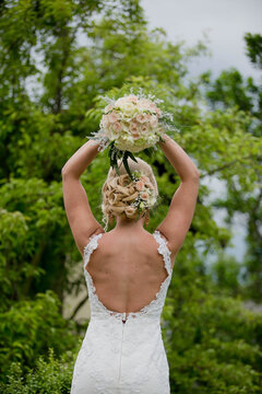 Shallow Focus Of A Young Blonde Bride Throwing A Bouquet Of Flowers In A Park