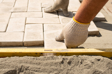 The master lays paving stones in layers. Garden brick pathway paving. Laying concrete paving slabs in house courtyard on sand foundation base - obrazy, fototapety, plakaty