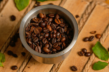A grinder with beans coffee inside it on a wood basket with leaves next to it close up detail setup