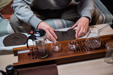 Obraz na płótnie Canvas Set for a tea ceremony close-up. A man using a tea needle breaks a tea cake of strong old ripe tea to enjoy the aroma