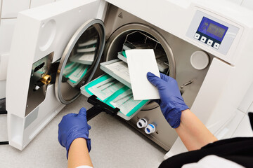 close-up of a doctor's hands in rubber gloves taking sterile instruments out of an autoclave.