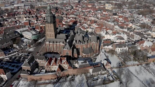 Aerial backwards movement with the Walburgiskerk cathedral of medieval Hanseatic Dutch tower town Zutphen in the Netherlands covered in snow with historic heritage cityscape