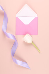 White tulip, silk ribbon and pink envelope on pastel pink background. Mockup with white card. Flat lay, top view.