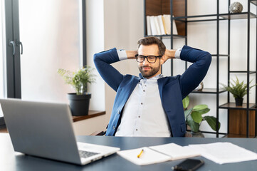 Successful bearded young businessman in business wear, glasses sitting at the desk at home office,...