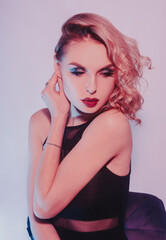 Fototapeta premium Fashion photo of young girl on Colored background, studio shot. Beautiful blond woman with red lips curly hair. Woman in neon light. The girl in body dancing go-go, night club. Sexy swimsuit
