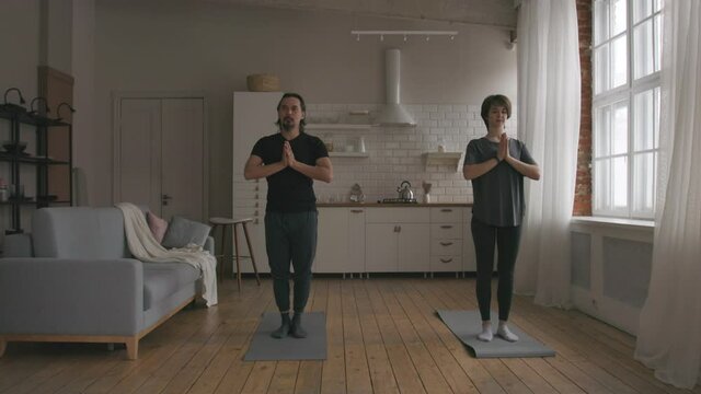 Man and Woman Practicing Yoga at home. Middle aged asian man practices yoga at his living room with his caucasian wife