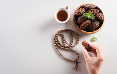 Top view image of decoration Ramadan Kareem background,  hands picking up dates fruit, tea and rosary beads. Flat lay background with copy space.