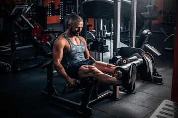Muscular man using weights machine for legs at the gym