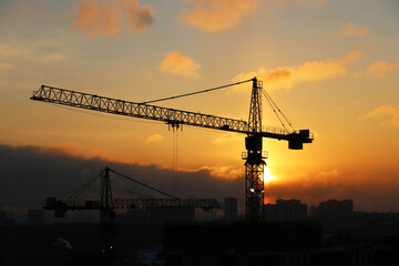 Silhouettes of construction cranes and residential buildings on sunrise background. Housing construction, apartment block in city