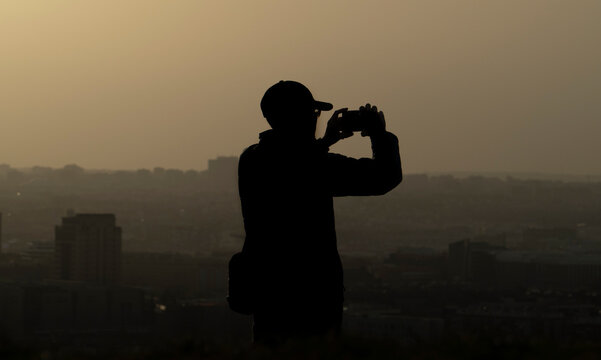 silueta negra de hombre con gorra al atardecer haciendo fotos al horizonte