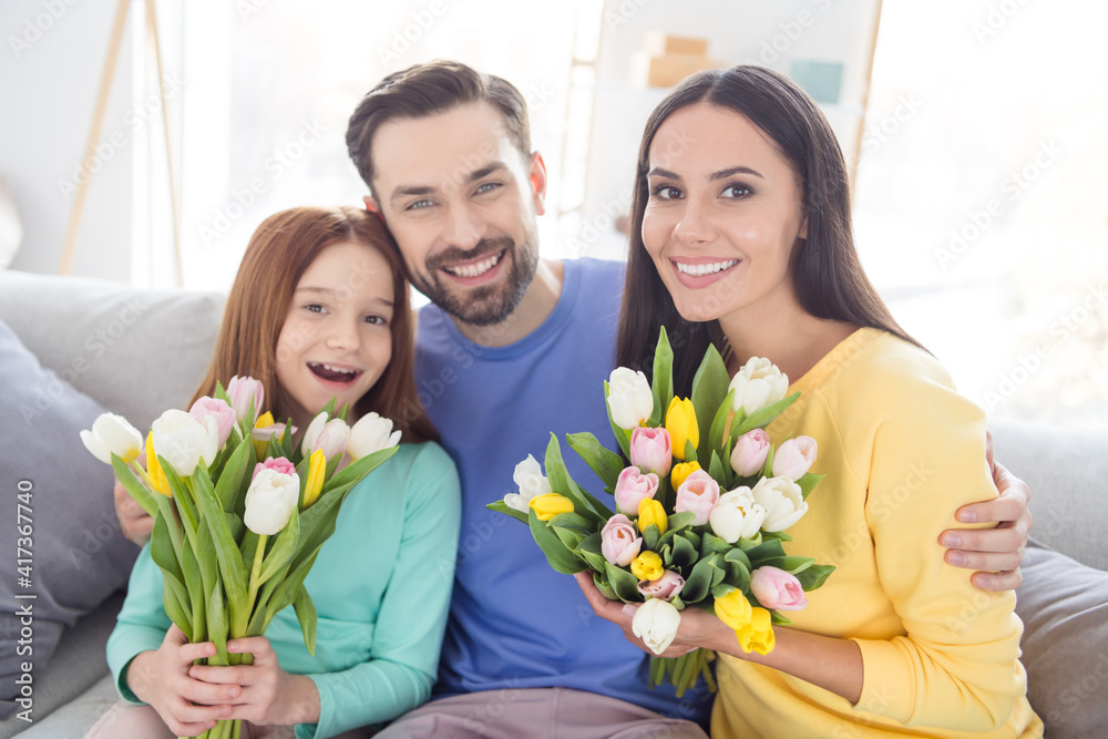 Sticker Photo of happy family hug cuddle enjoy time together positive smile girls hold flowers bouquet spring sit couch home