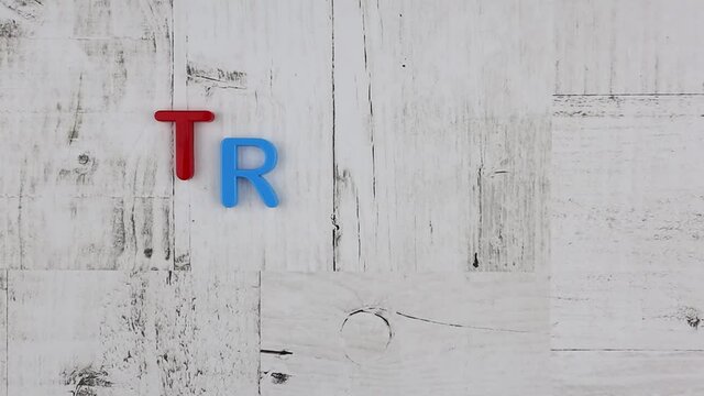 Word - Travel - in bright colorful letters arranged diagonally on grey wood background with corner borders with a multicolored alphabet. Stop motion, top view