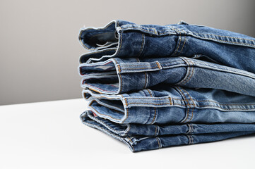 A set of folded jeans on white table, side view. Wardrobe in the casual style. Collection of jeans.