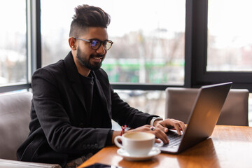 Young indian man holding phone while sitting at his working place in cafe.