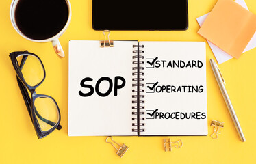 SOP - Standard Operating Procedure, text on notepad and office accessories on yellow desk.